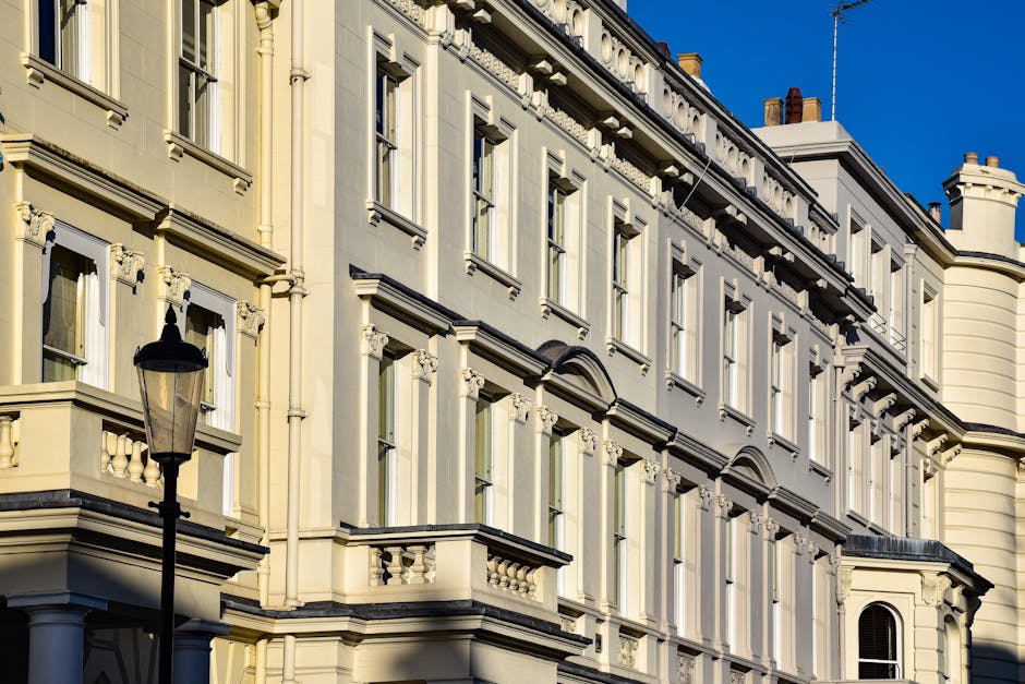 A detailed view of a classic, multi-story residential building with ornate architectural features, including large rectangular windows with decorative moldings, creamy-yellow exterior walls, and black